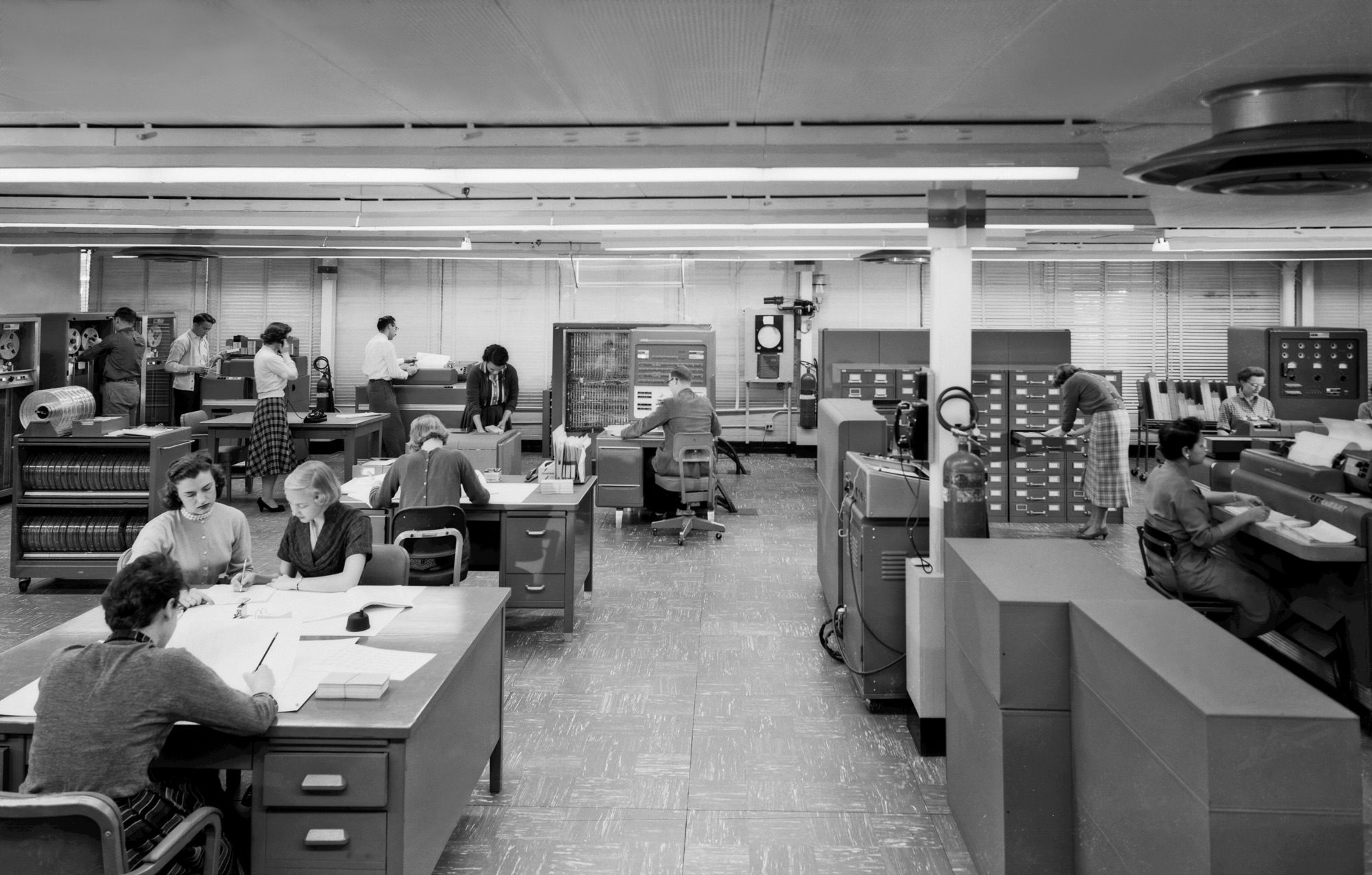 A 1957 computer room: operators at desks and tape units around an IBM 704.