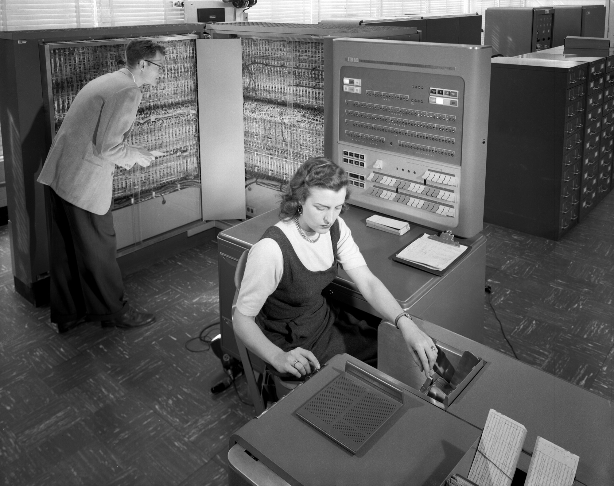 An operator at the console of an IBM 704 while an engineer works inside an open cabinet.